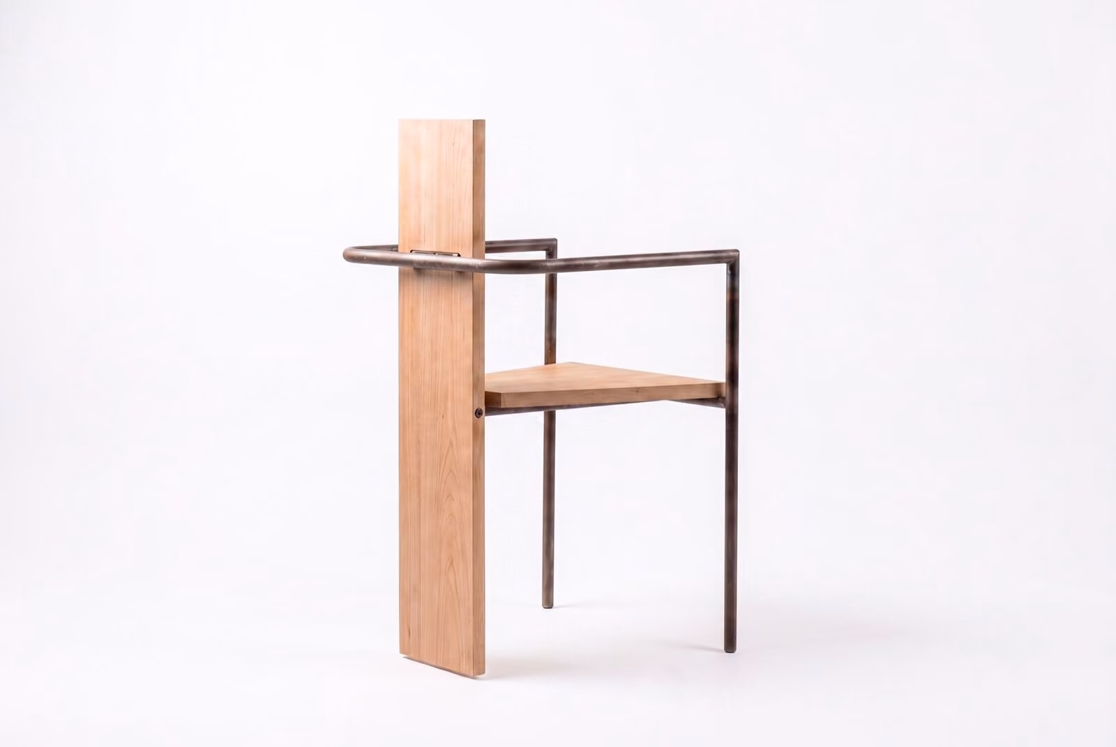 Through-Fixed: A solid wood plank stands as the vertical backrest, crossed by a bent steel tube frame that shapes the arms and continues down into the front legs